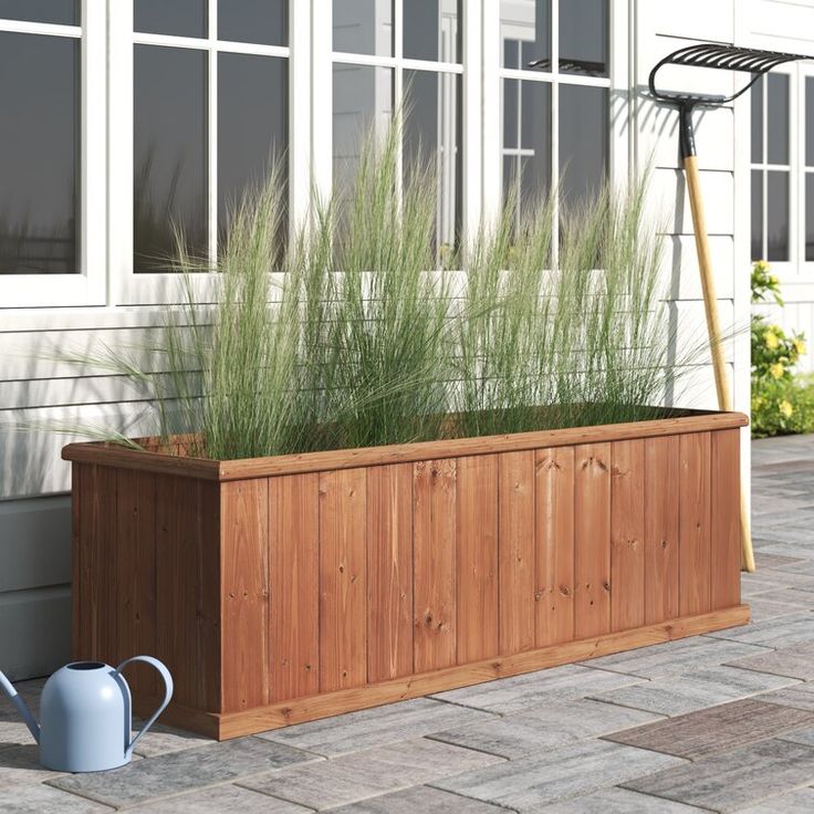 a wooden planter with grass in it next to a watering can on the side of a house