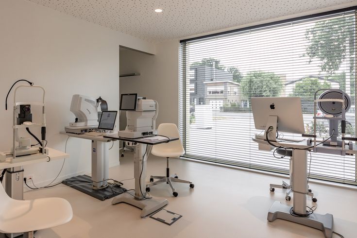 an office with multiple computers on desks and chairs in front of large windows that look out onto the street