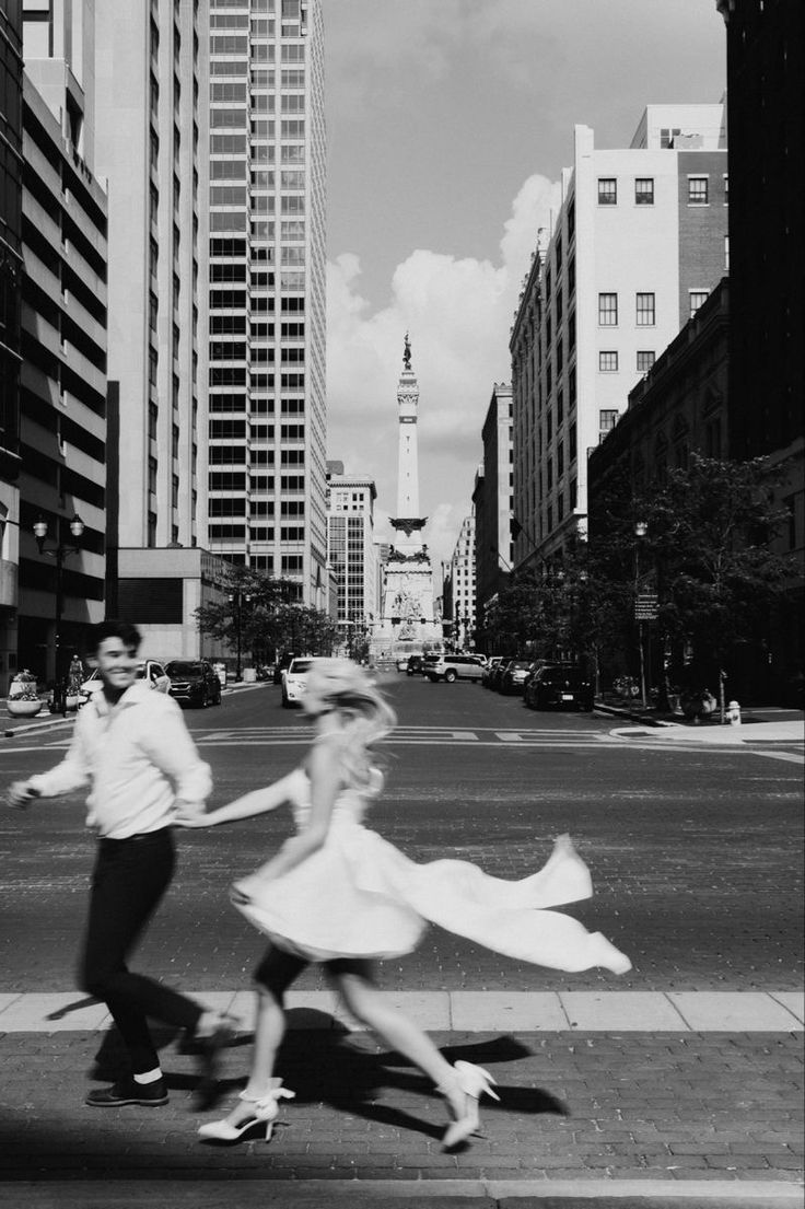 black and white photograph of two people crossing the street in front of tall buildings with skyscrapers behind them