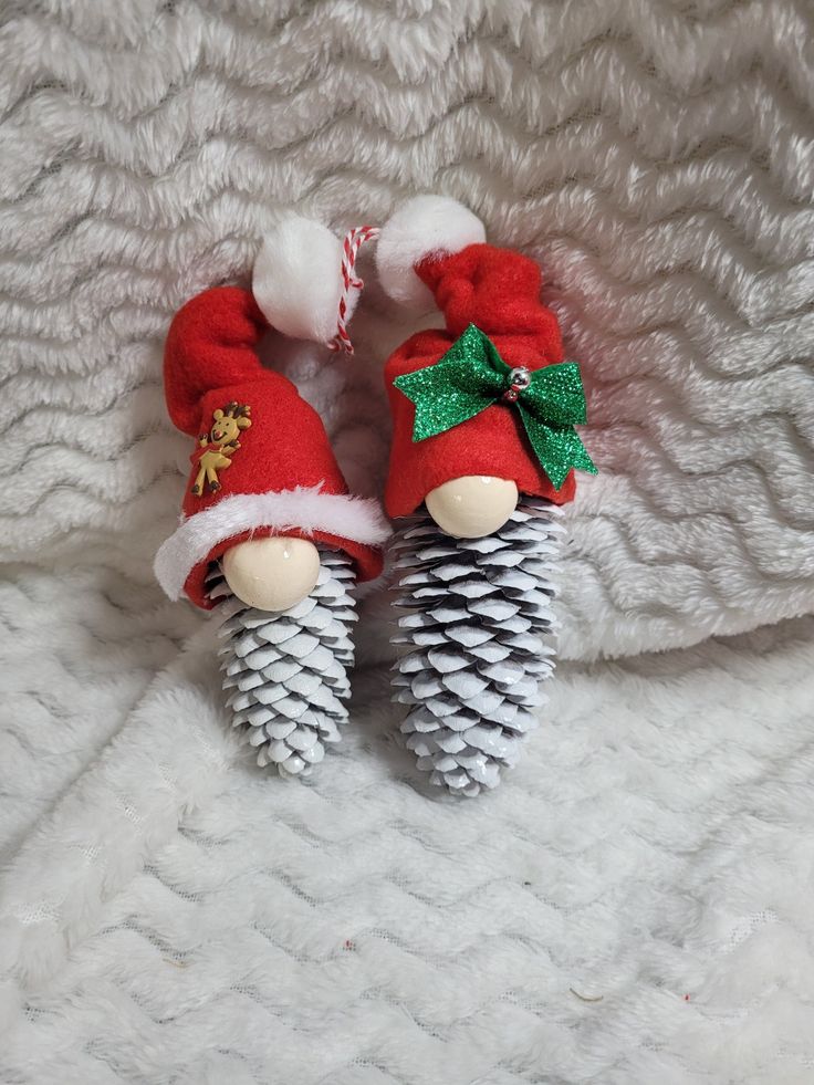 two pine cones with santa hats on them are laying on a white fur covered surface