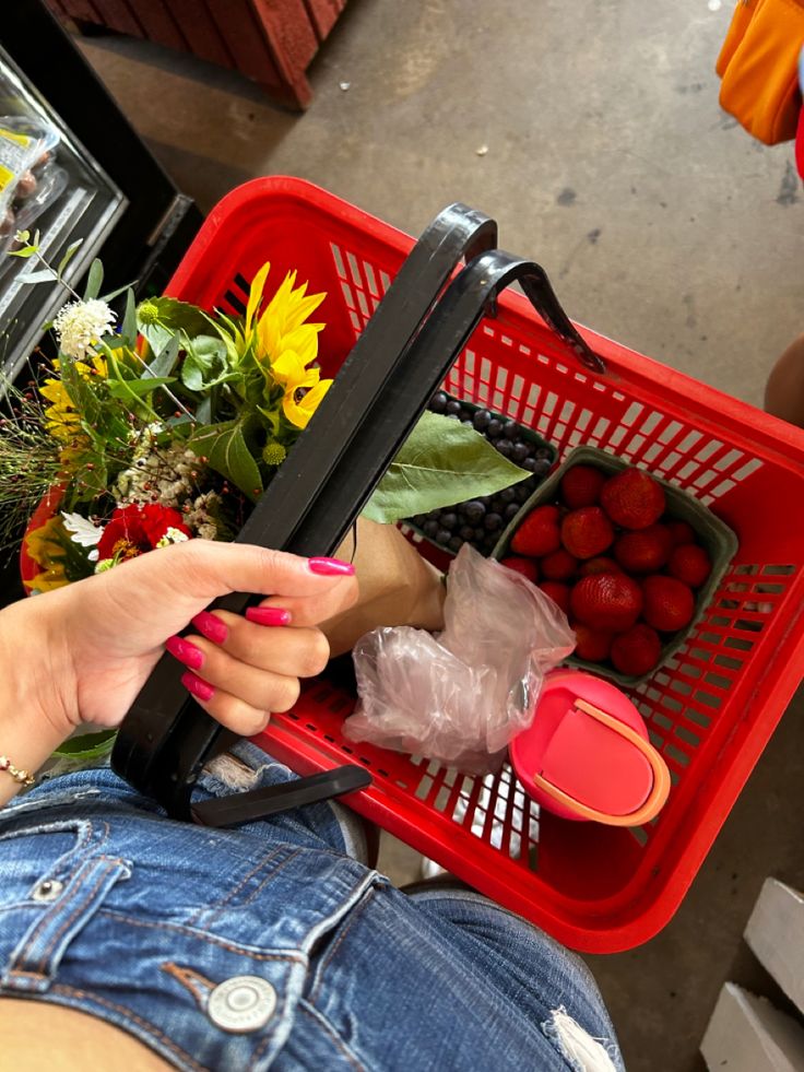 a woman holding a shopping basket full of fruit and vegetables