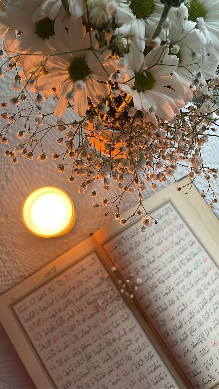 a vase filled with white flowers sitting next to an open book on top of a table