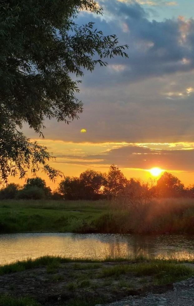 the sun is setting over a river in an open field with grass and trees on either side