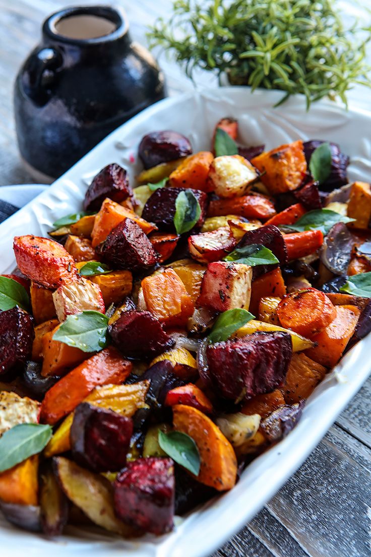 a white platter filled with roasted vegetables on top of a wooden table next to a potted plant