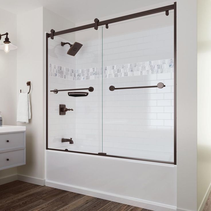 a bathroom with white tile and black fixtures on the shower wall, along with dark wood flooring