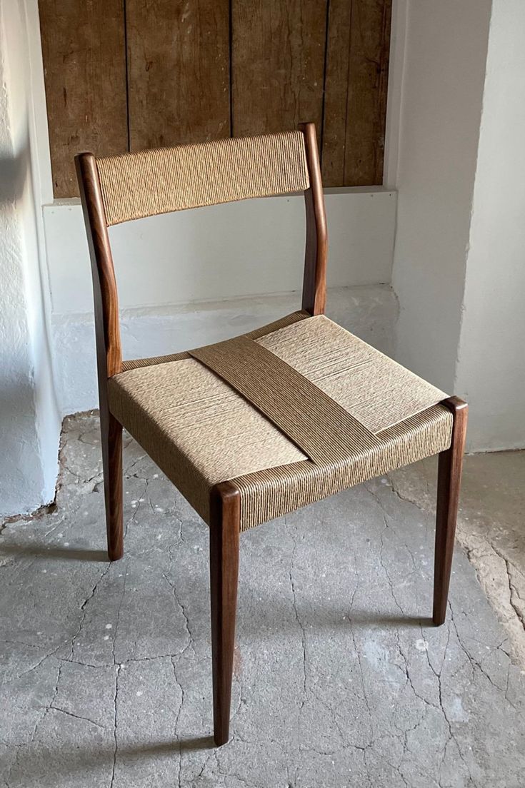 a wooden chair sitting on top of a cement floor next to a white wall and door