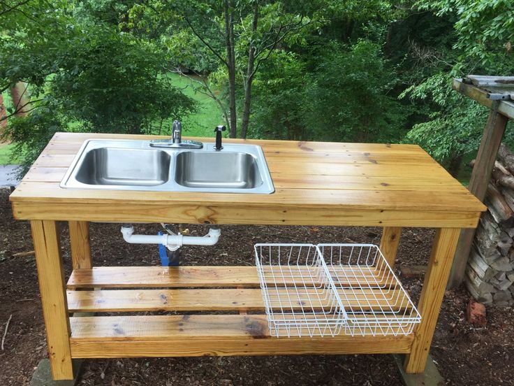 a wooden table with two sinks on it in the middle of some dirt and trees