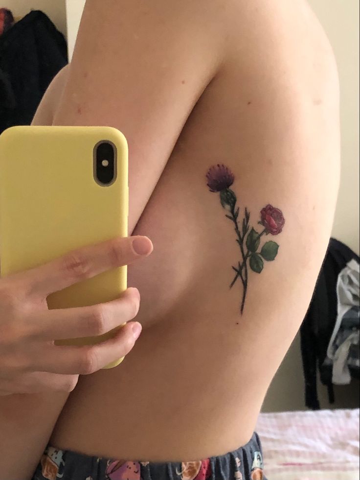 a woman with a flower tattoo on her arm holding a cell phone in front of her