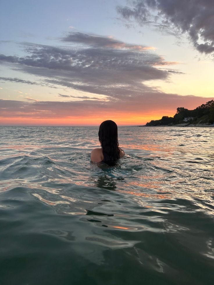 a woman is swimming in the ocean at sunset with her back turned to the camera