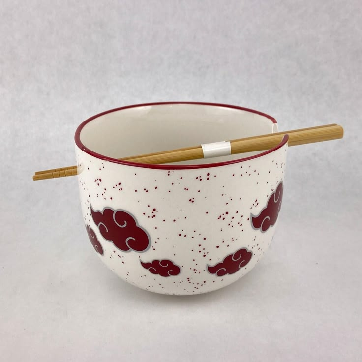 a red and white bowl with chopsticks sticking out of the top in front of it