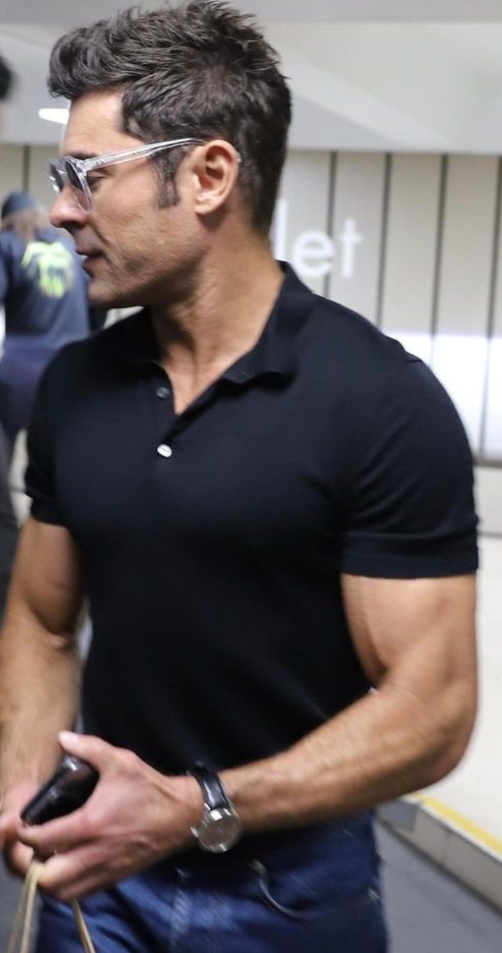 a man in black shirt and glasses holding a cell phone while walking through an airport