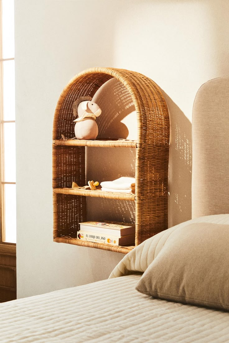 a wicker shelf on the side of a bed next to a pillow and pillows