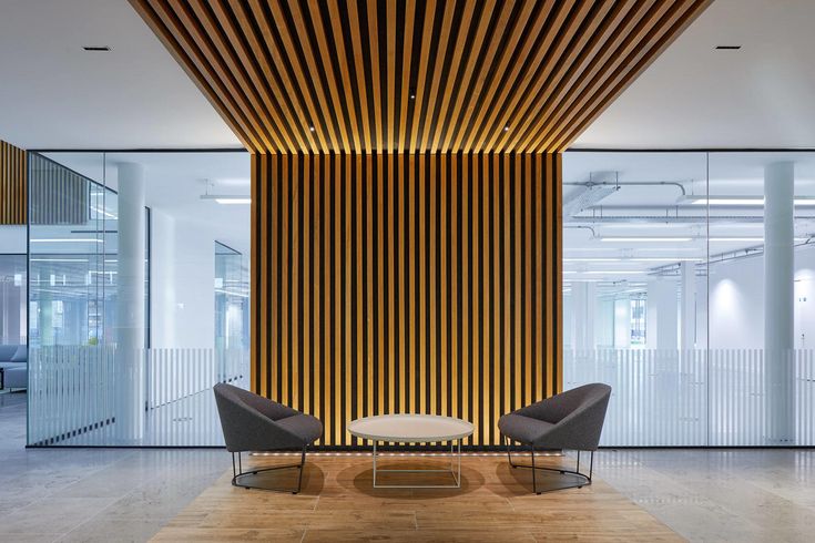 an office lobby with two chairs and a coffee table in front of a wooden wall