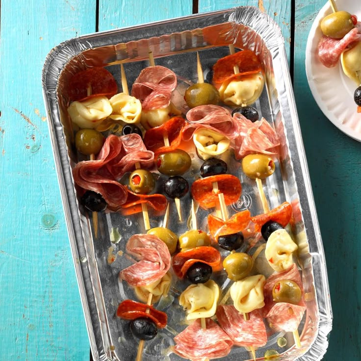 a tray filled with different types of appetizers on skewers next to a plate of olives and ham