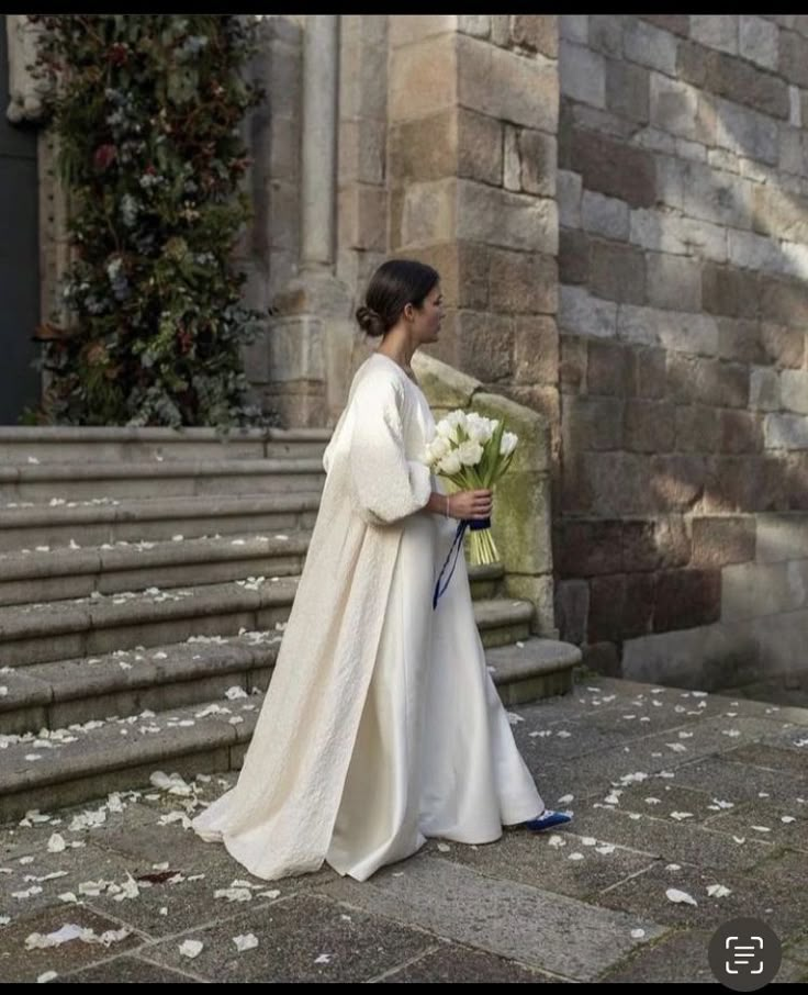 a woman in a white dress is walking down the street with flowers on her lap