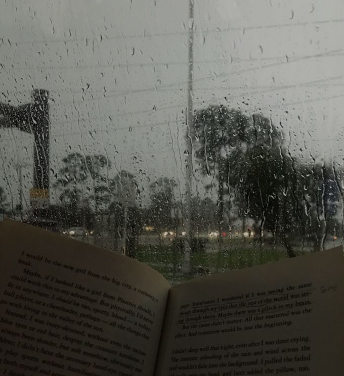 an open book sitting on top of a window next to a rain covered street sign