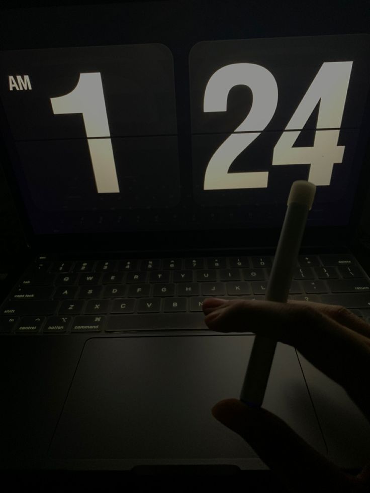 a person holding a pen in front of a laptop computer with the time displayed on it