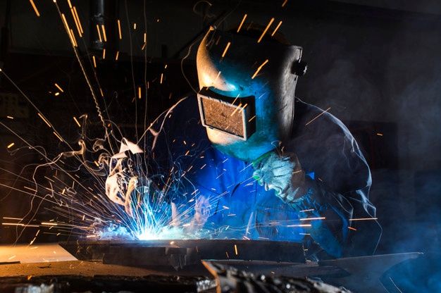 welder cutting metal with sparks in the air and blue light coming from his face