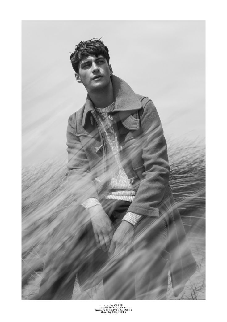 a young man sitting on top of a beach next to the ocean in black and white