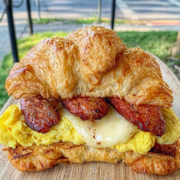 a croissant sandwich with bacon and eggs on it sitting on top of a wooden table