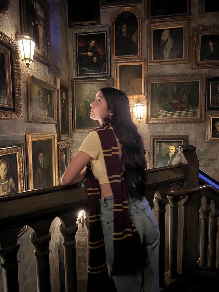 a woman is standing on the stairs looking up at some paintings and lights above her