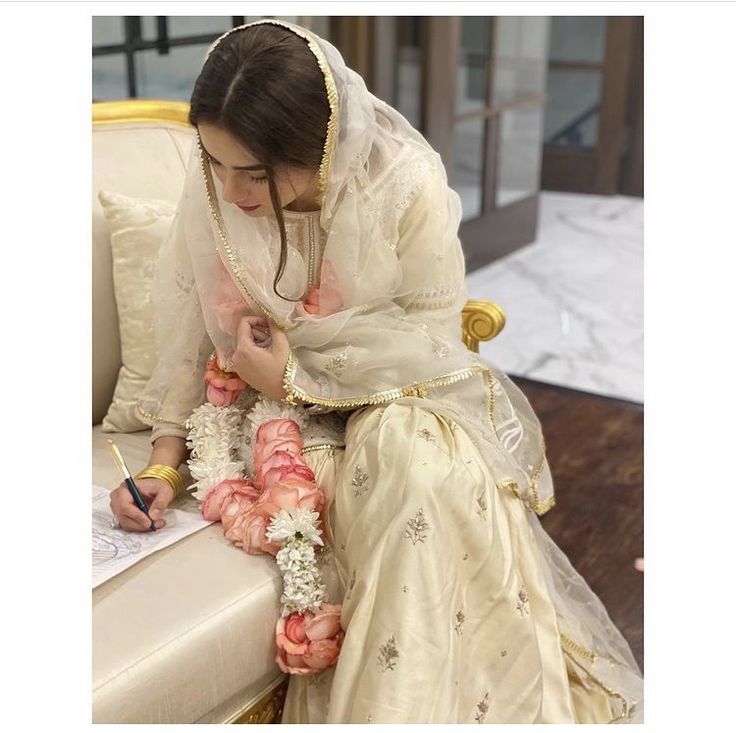 a woman is sitting on a couch writing in her wedding dress and getting ready to sign the marriage register