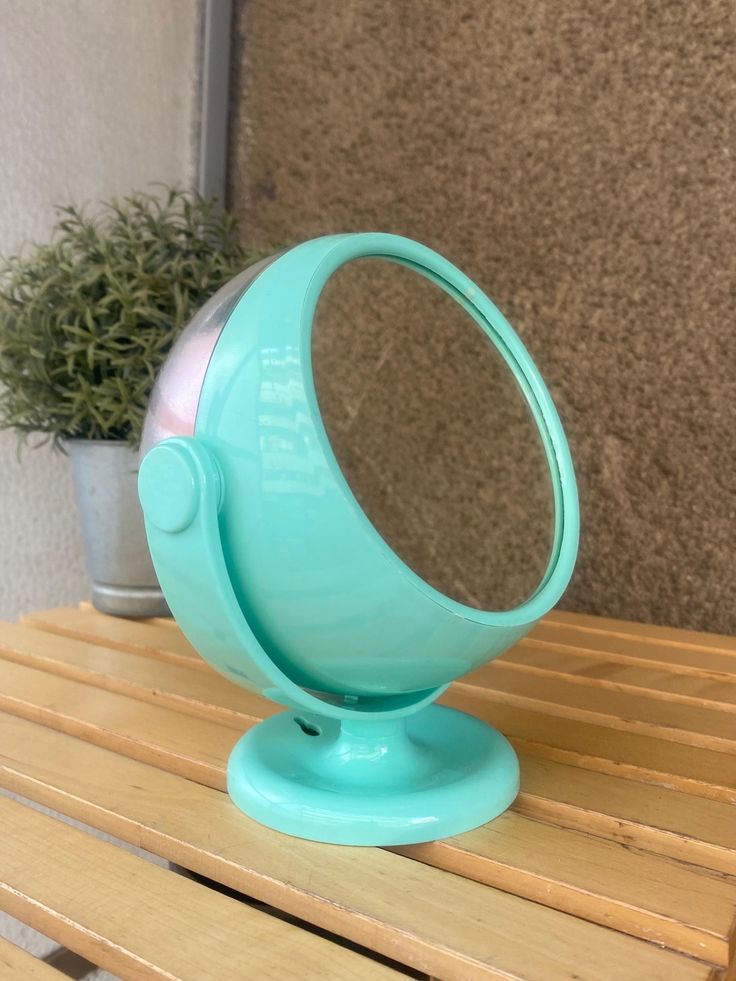 a blue ball shaped mirror sitting on top of a wooden table next to a potted plant