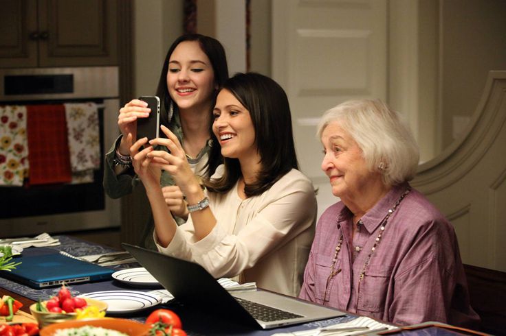 three women sitting at a kitchen table taking pictures with their cell phones and laptops