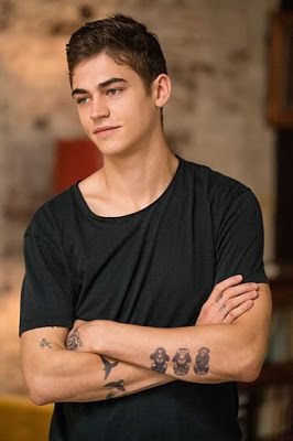 a young man with his arms crossed looking at the camera and wearing a black t - shirt