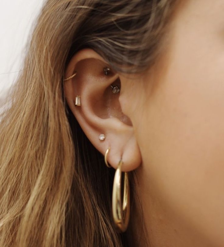 a close up of a person with ear piercings on their ears and wearing gold hoop earrings