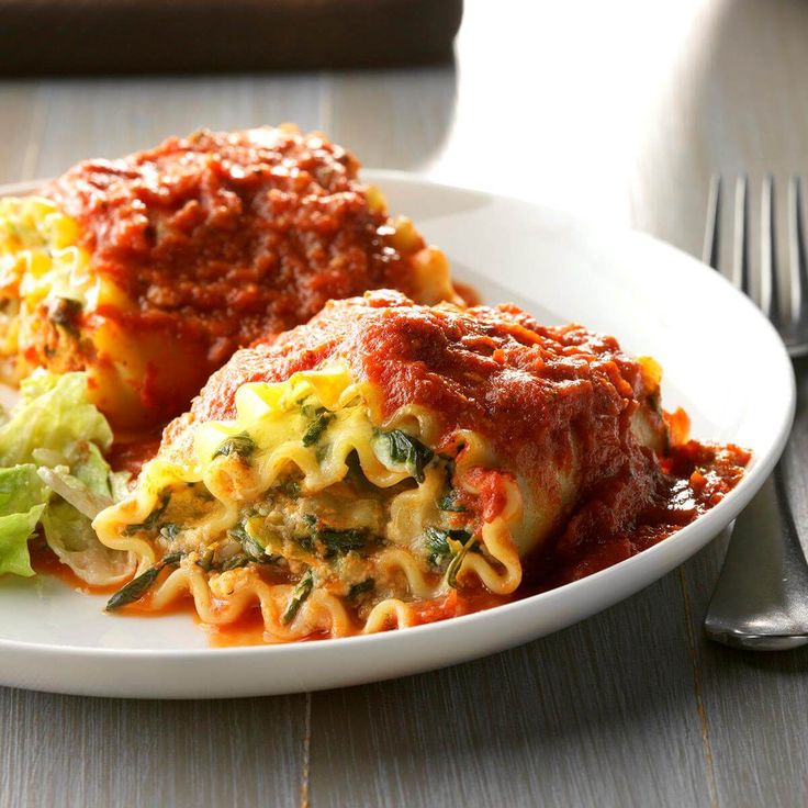 a white plate topped with lasagna covered in sauce and vegetables next to a fork