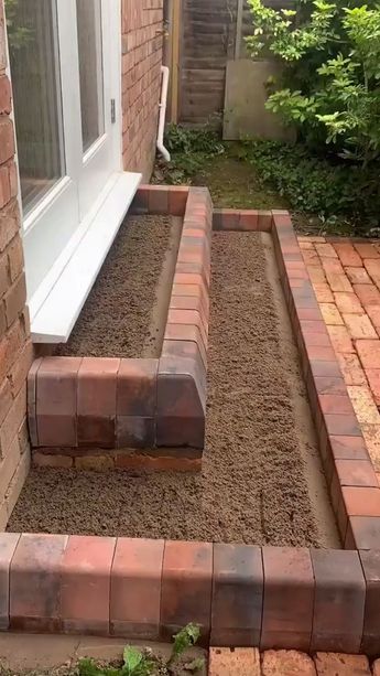 a brick garden bed in front of a house with grass growing on the ground next to it