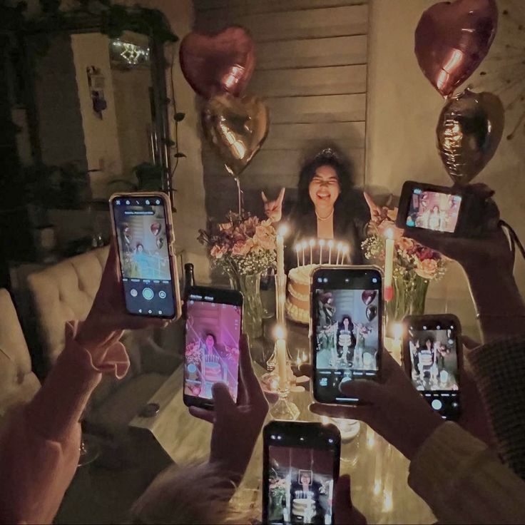 a group of people holding up cell phones in front of a table with balloons and candles