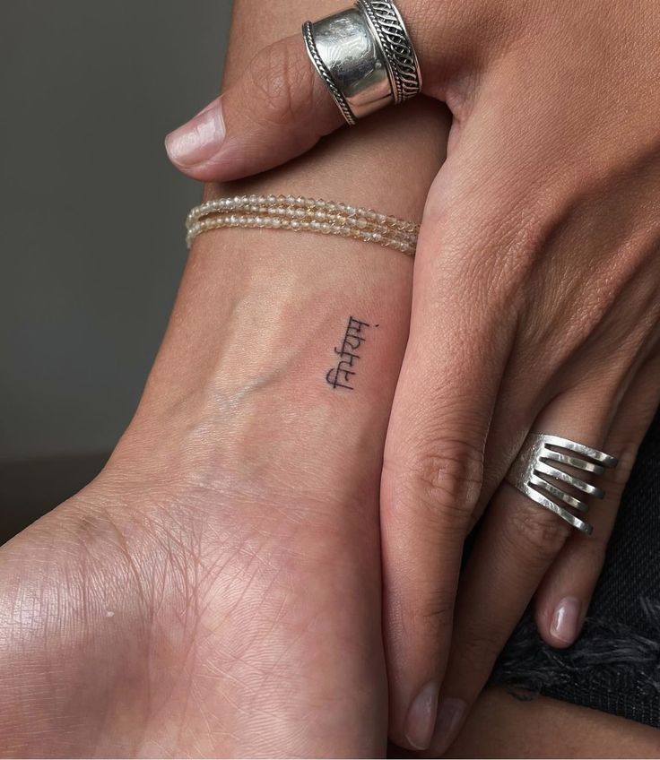 two people are holding hands with tattoos on their wrists and wristbands, one has the word faith written in cursive letters