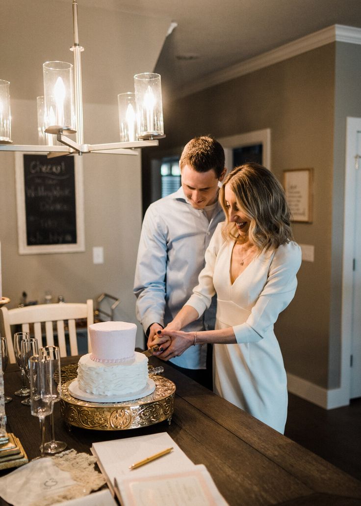 a bride and groom cutting their wedding cake at the reception table in front of an elegant chandelier