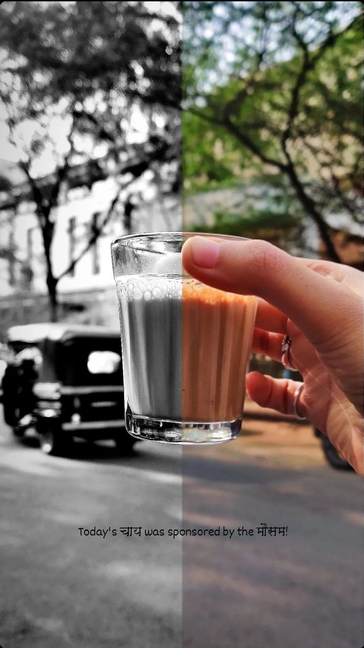 a hand holding a glass filled with liquid on top of a street next to parked cars