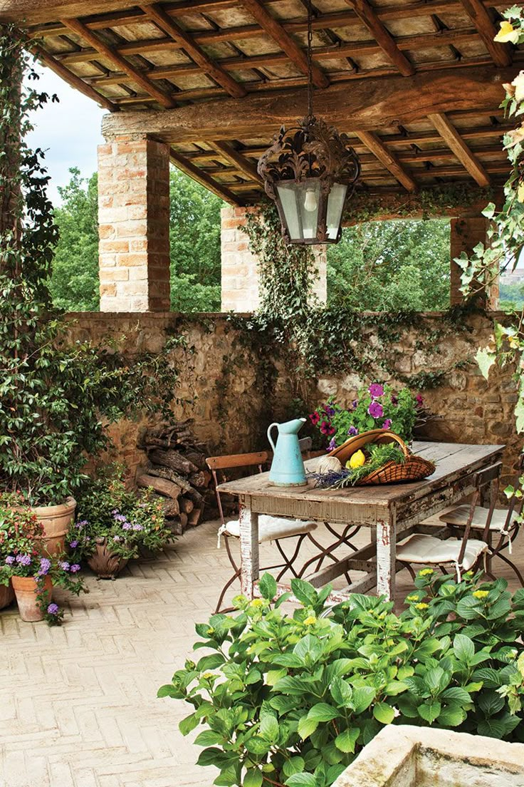 an outdoor dining area with potted plants on the table and hanging lights above it