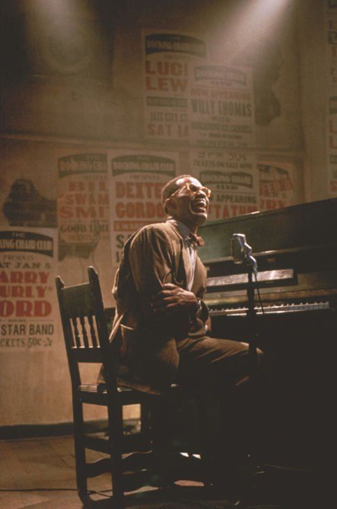 a man sitting at a piano in front of a microphone and posters on the wall