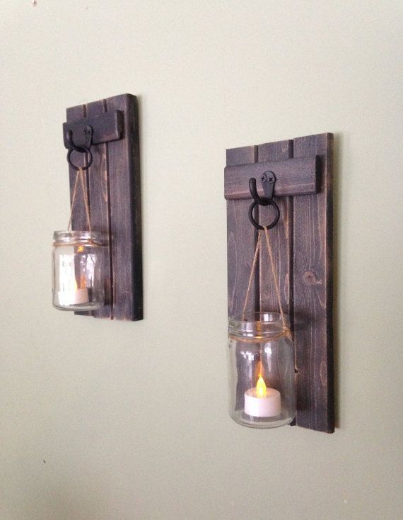 two mason jars are hanging on the wall with candles in them and one candle is lit