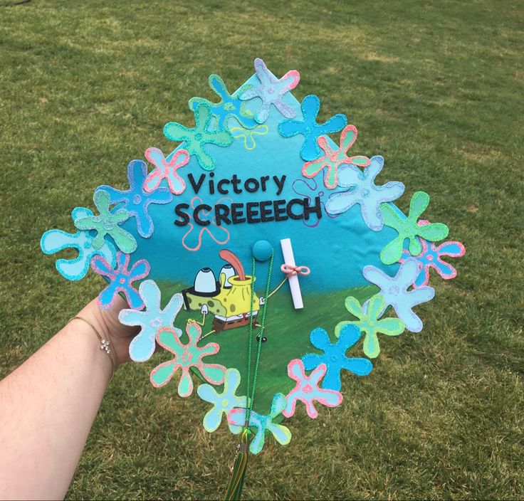 a hand holding up a fake victory street sign in the grass with flowers on it