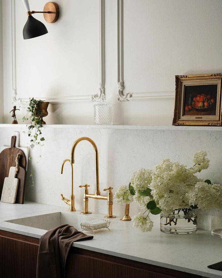 a kitchen sink with gold faucets and white flowers on the counter top next to it