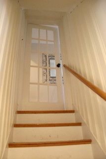 the stairs lead up to an open door in a house with white walls and wood handrails