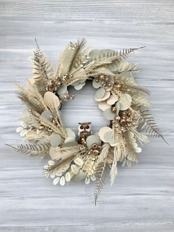 a wreath made out of dried leaves and feathers with an owl on it's head