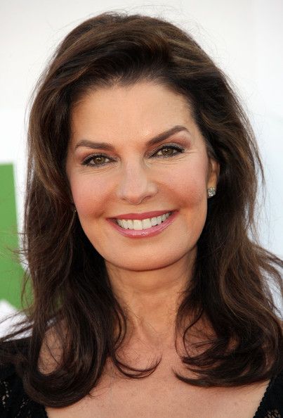 a woman with long brown hair smiling at the camera and wearing a black dress in front of a white background