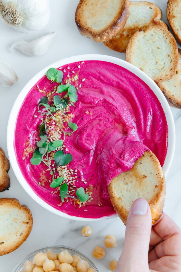 a bowl of hummus with bread and sprinkles next to garlic on the side