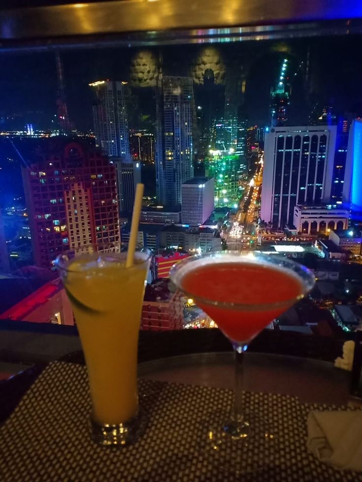 two drinks are sitting on a table in front of a cityscape at night