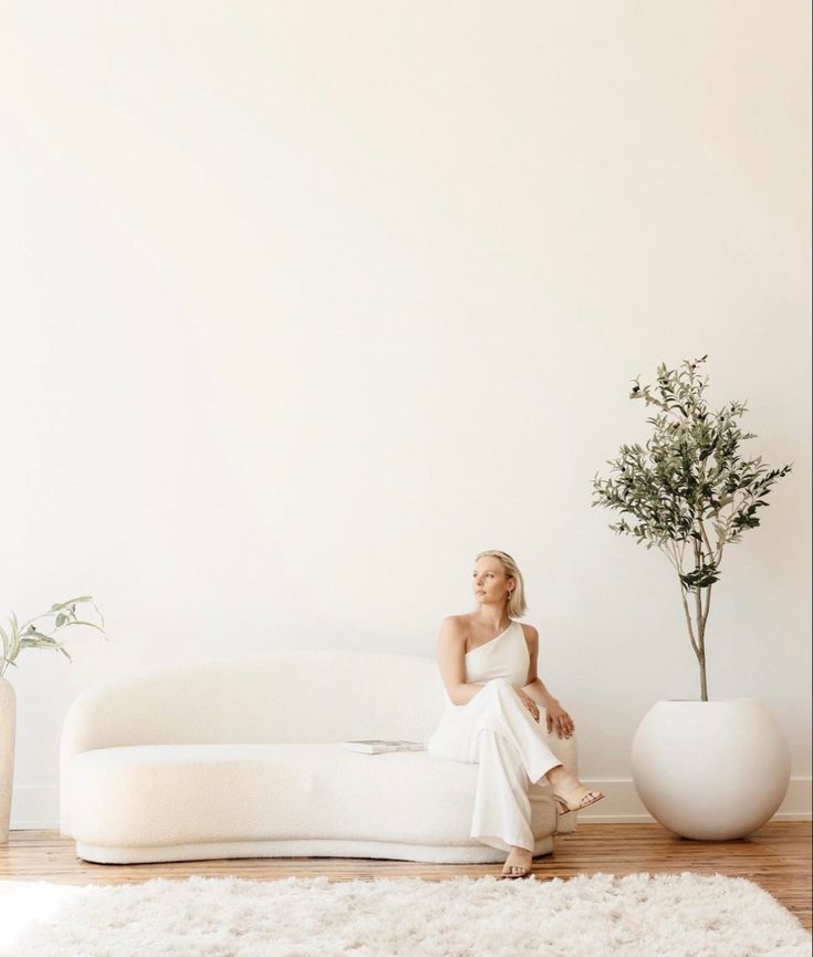 a woman sitting on top of a white couch next to a potted plant