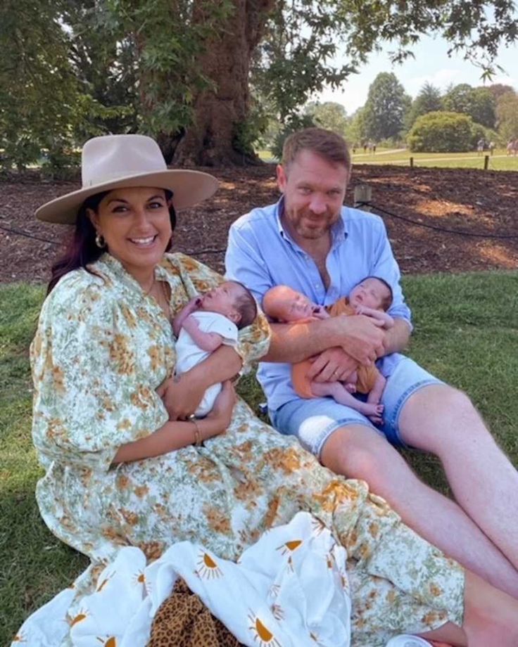 a man and woman are sitting on the grass with their baby in their arms,