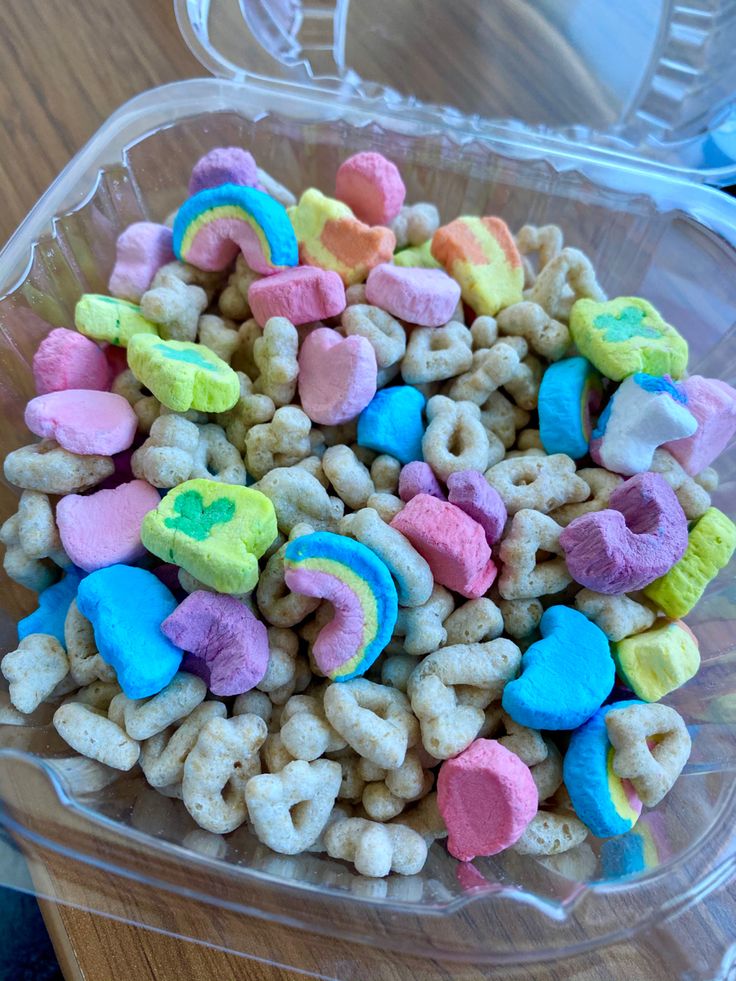 a plastic container filled with cereal and rainbow colored candies on top of a wooden table