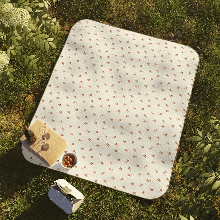 a picnic blanket and some food on the ground in the middle of green grass with flowers